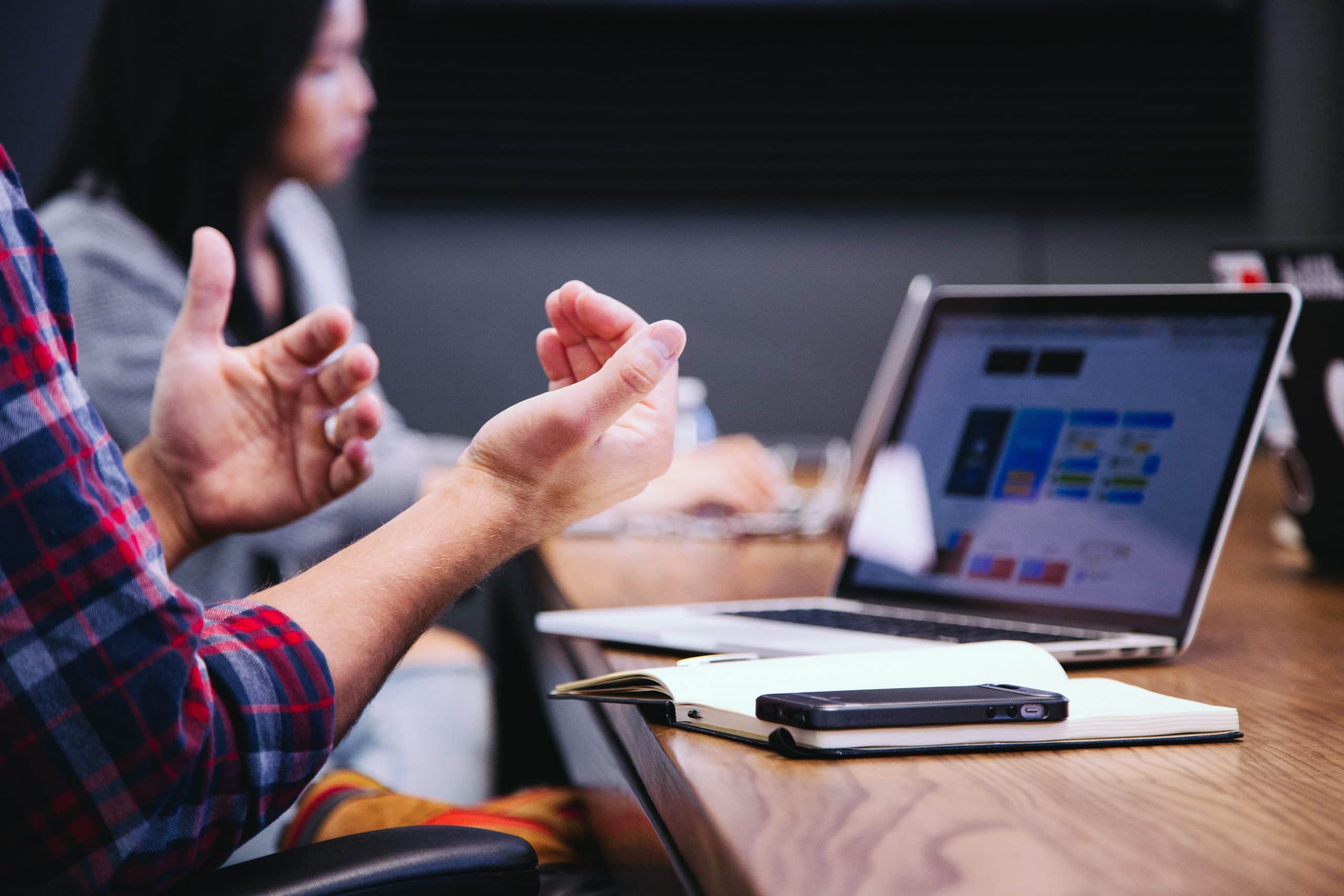 Photo of a man working at his laptop with another women also working in the background