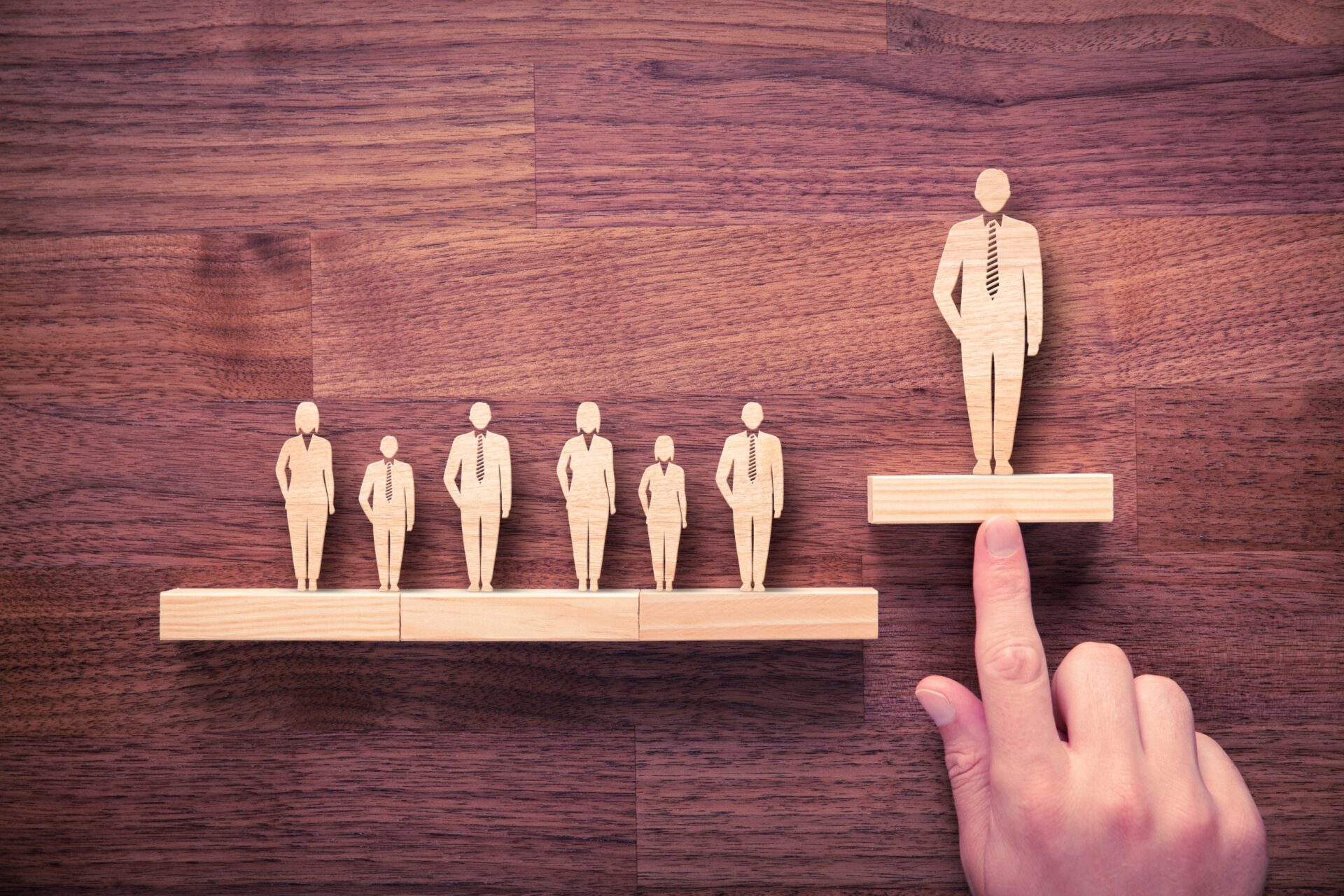 Photo of wooden people with one higher than the others, representing the leader