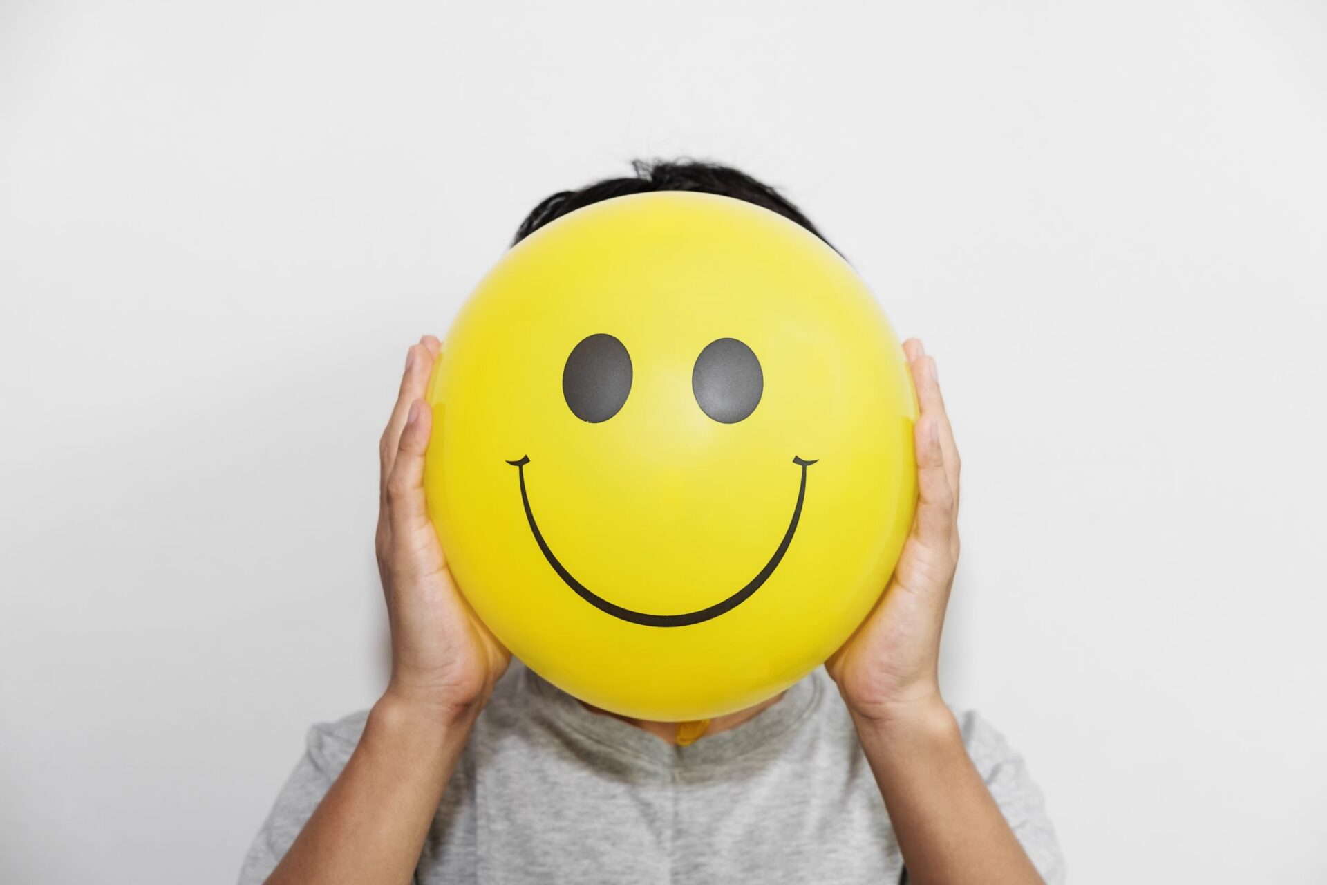 Photo of someone holding a yellow smiley face over their own face