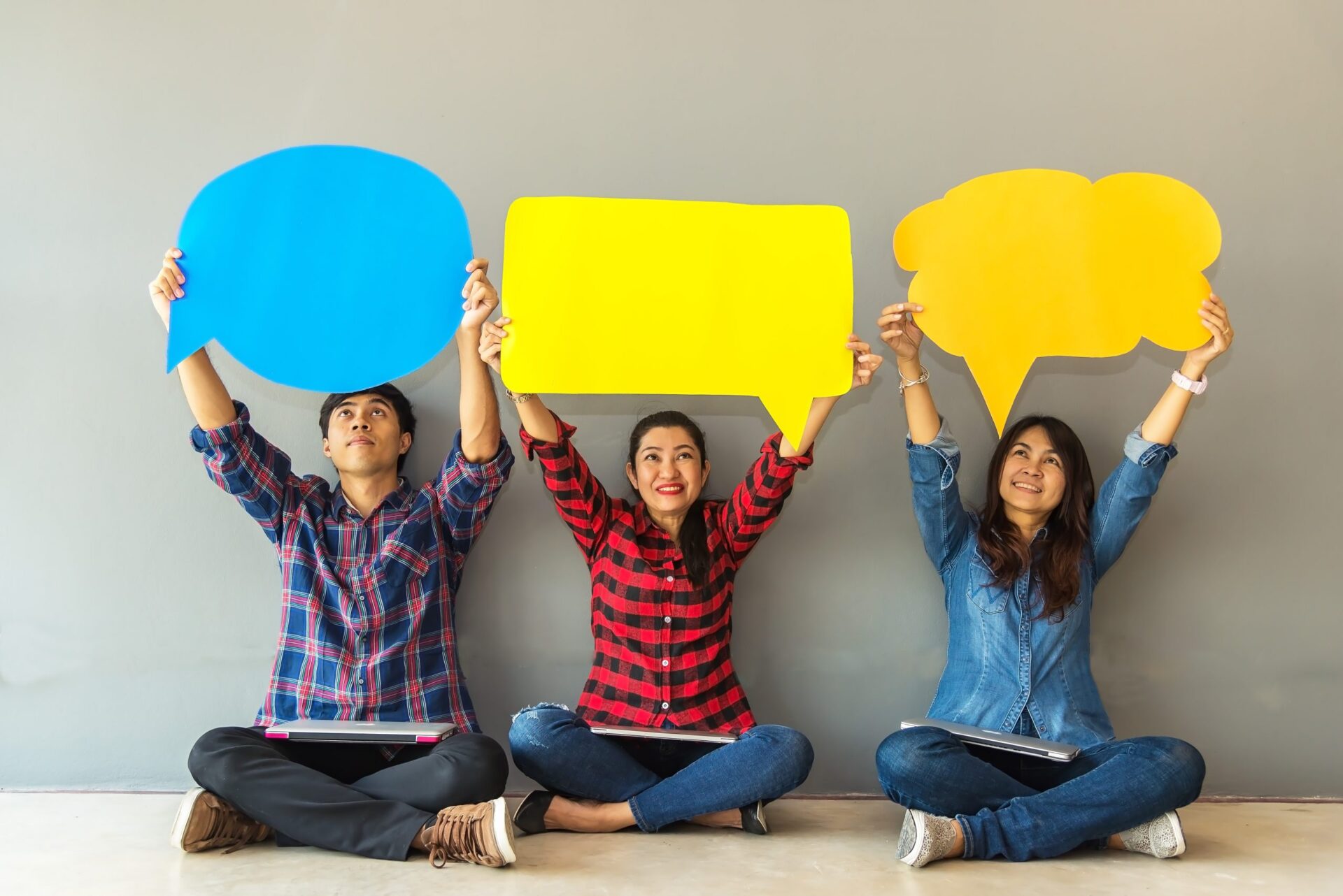 Photo of three people holding up speech and though bubbles