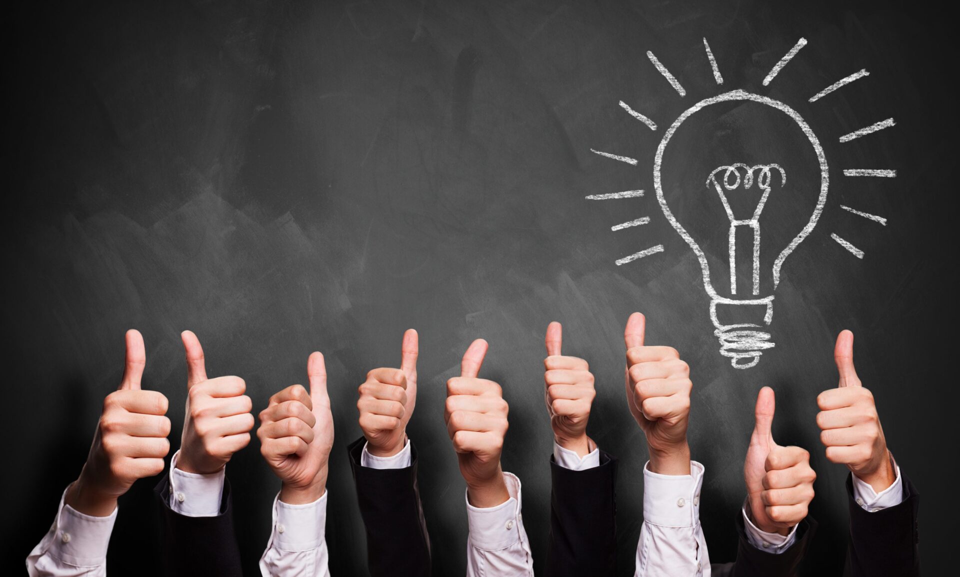 People with their thumbs up infront of a blackboard with a light bulb drawn on in chalk